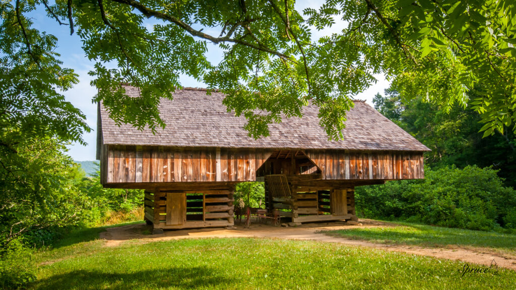 Cantilever barn in Cades Cove framed by walnut tree branches in the foreground.